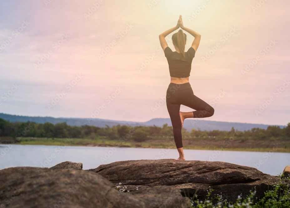 Woman in yoga pose on rocks next to the lake.